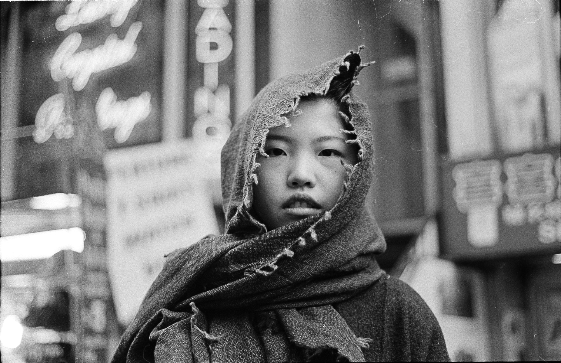 Black and white portrait of a girl wrapped in a scarf under neon signs