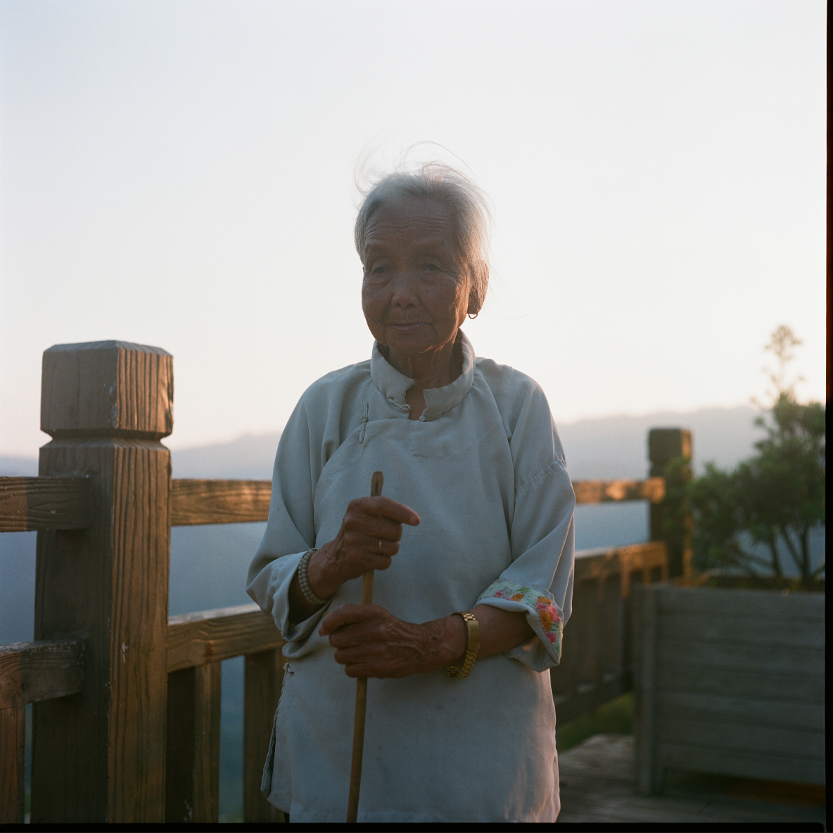 Portrait of an elderly woman holding a cane, backlit by golden light